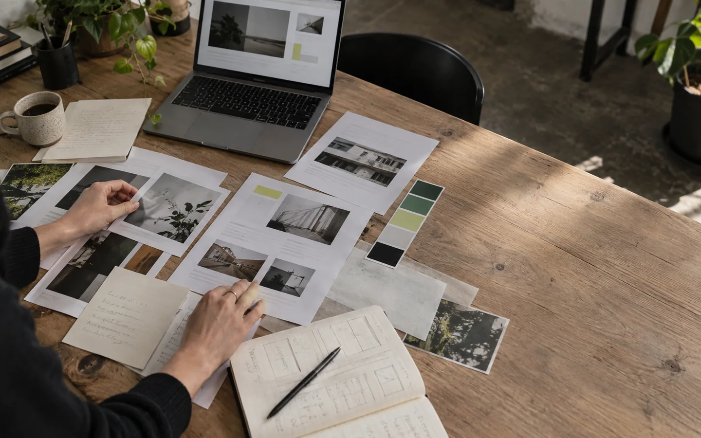 Hands arranging page layouts, notes and colour samples on a website planning desk